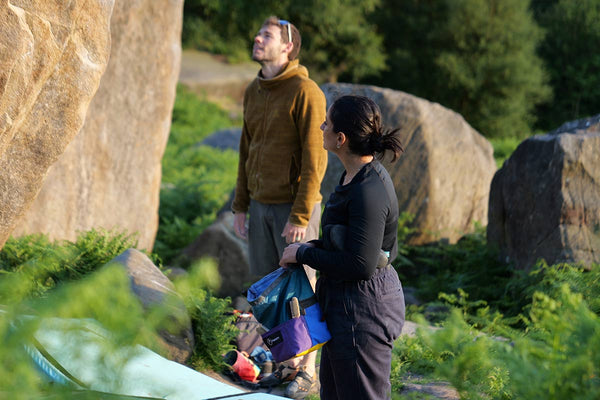 A boulderer standing on a bouldering pad crash mat next to a white bouldering chalk bag at rubicon crag in the peak district