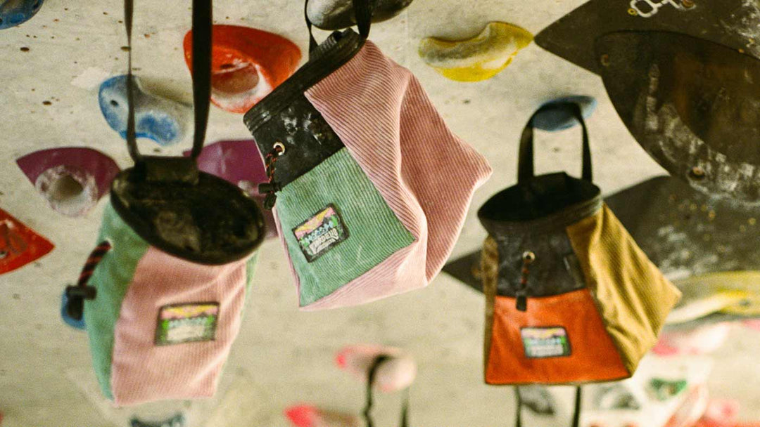 A selection of bouldering buckets and climbing chalk bags hang from hand holds on a boulder wall at Parthian Climbing in Manchester