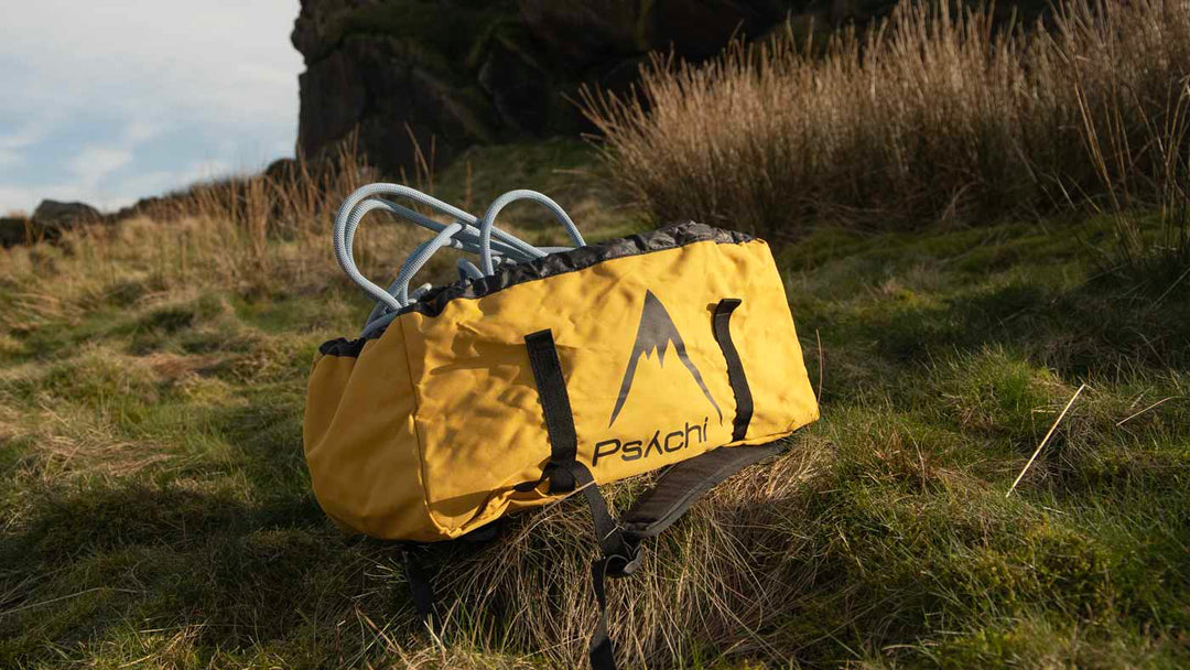 A yellow rope bag containing a blue climbing rope sits in front of a boulder at Cratcliffe Crag in the Peak District