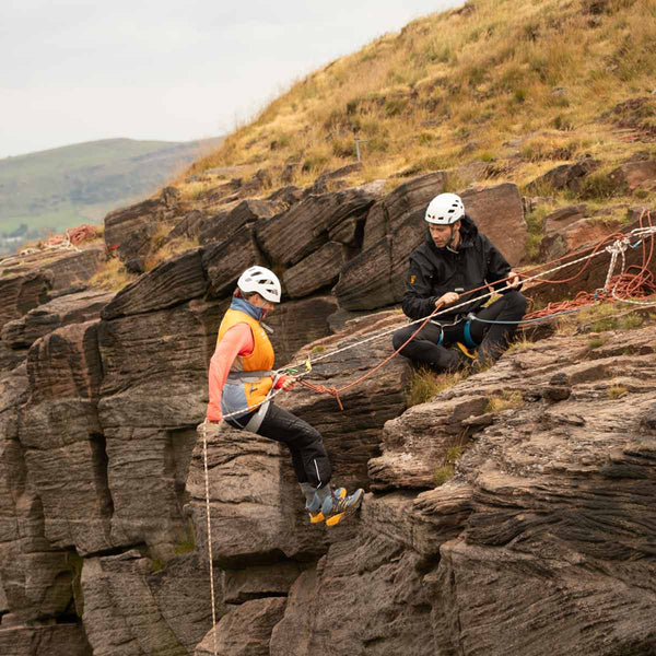 A climbing instructor supervising as a beginner climber begins abseiling off a cliff edge at Bamford Edge in the Peak District.