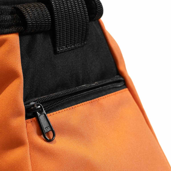 A light orange and black bouldering chalk bucket with drawstring closure and zip closure climbing accessory pockets