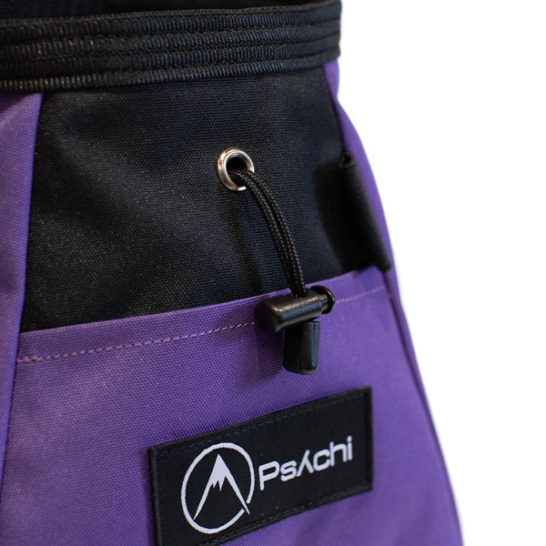 A purple and black bouldering chalk bucket with drawstring closure and climbing accessory pockets
