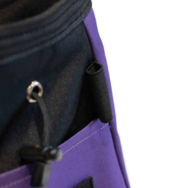 A purple and black bouldering chalk bucket with drawstring closure and climbing brush holder