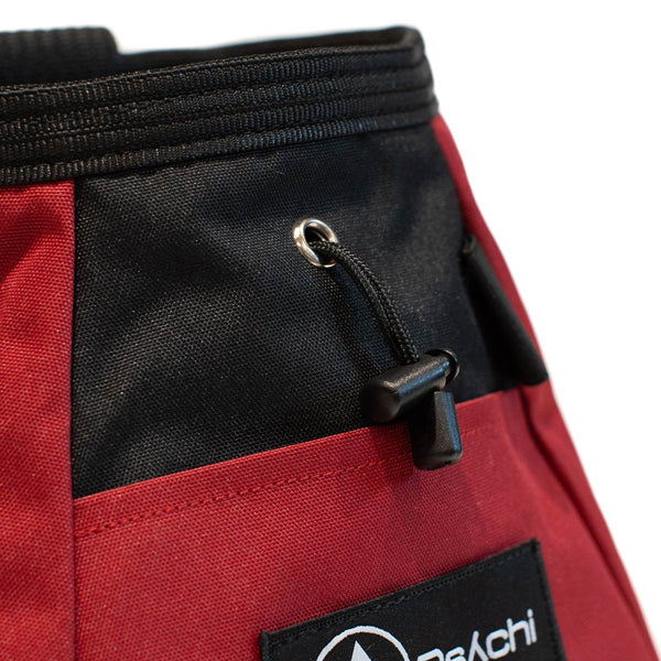 A red and black bouldering chalk bucket with drawstring closure and climbing accessory pockets