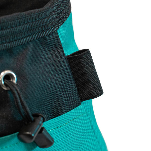 A turquoise and black bouldering chalk bucket with drawstring closure and climbing brush holder