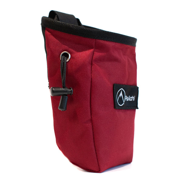 A red rock climbing chalk bag with drawstring closure and Pyschi white mountain logo on a black fabric patch