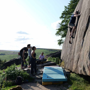 A group of 4 boulderers watch on as a climber climbs up a boulder face at Stanage Edge in the Peak District.