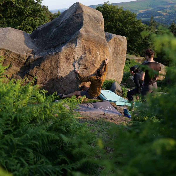 A boulderer clings to a rock at Stanage Plantation in the Peak District as two friends watch on.