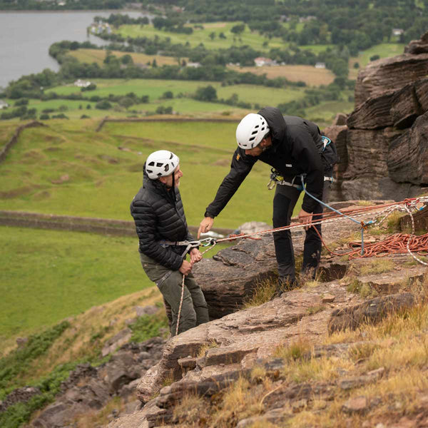 A climbing instructor explaining a saftey harness rig to a beginner climber as they begin abseiling of a rock ledge at Bamford Edge in the Peak District.