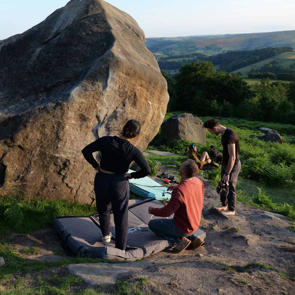 A climbing instructor places a bouldering crash pad below a boulder at stanage plantation in the peak district.